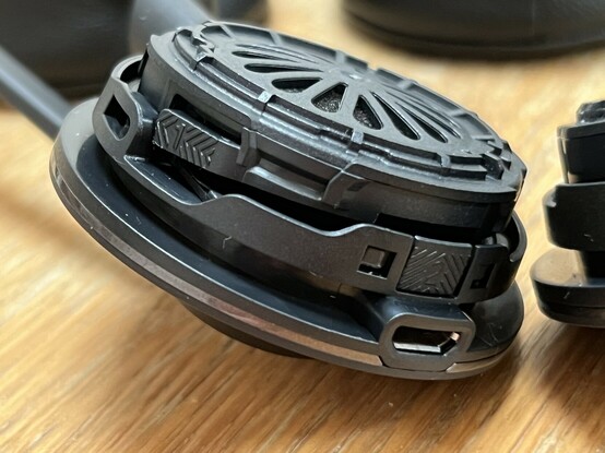 The main headphone of the Engage 55, with the ear cushion removed revealing a black plastic speaker and two little clips with the numbers 1 and 2 with chevron arrows to show you what order and direction to open the battery compartment.