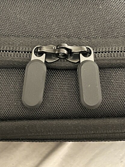 Zip. Two oval, black pull tabs coating a black painted zip. The photo is weird and makes it look gunmetal grey. It’s not gunmetal grey. The zipper looks pretty good quality and there’s a loop for a tiny padlock.