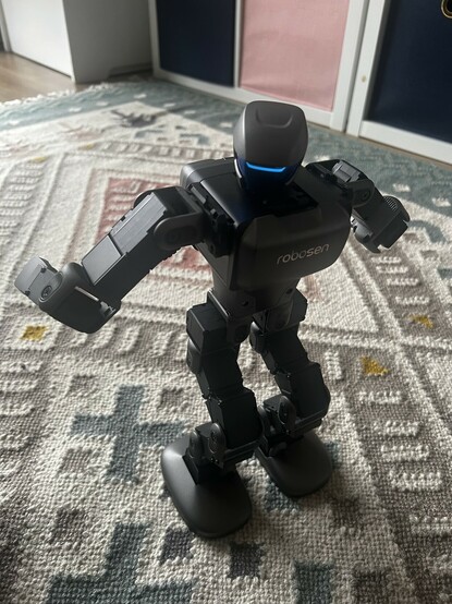 A small, grey and black, sophisticated toy robot doing a bit of a wiggle.