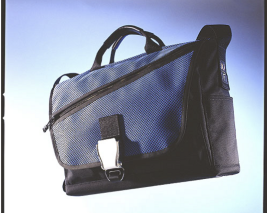 A magazine scan of a photo of a black messenger bag with a blue mesh flap. It has a metal buckle and a jaunty diagonal zip pocket. It's clearly an old photo- probably from circa 1998/1999.
