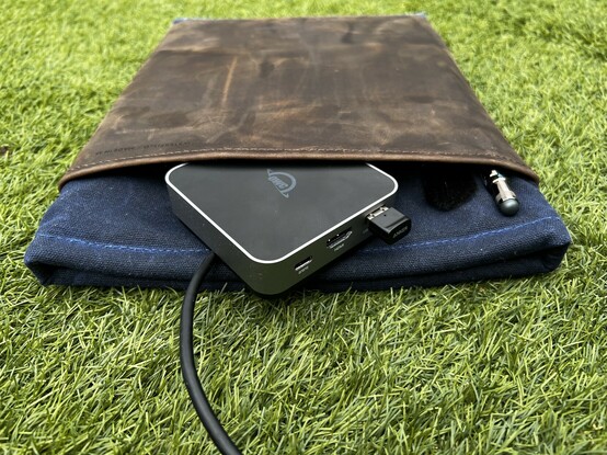 The square, thick OWC Travel Dock E sticking out of a WaterField Designs laptop folio pouch. It will not fit in the front pockets.