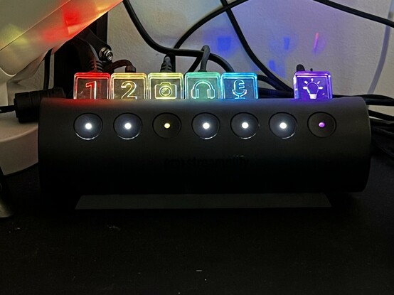 A round USB hub with seven buttons along the front. Five are illuminated to indicate they’re turned on. Little plastic tabs stick out of the top and are edge lit in rainbow colours. They have icons indicating what device is plugged in, approximately anyway.