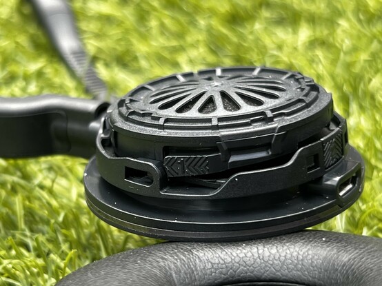 Closeup of the Jabra Engage 55 ear cup, showing a little tab with chevron style arrows and a number 1 on it. You’re supposed to push it down and move the ear cup in the direction of the arrows, swinging it open.