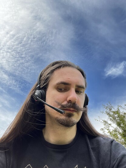 Me, set against a blue sky dimpled by clouds. I’m sporting the Jabra Engage 55 headset with the microphone boom down, and giving it side-eye.