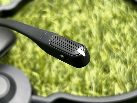 A tiny little microphone boom set against blurred, green grass. A little mute button and status LED are visible.