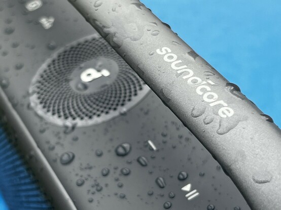 A close up of the Motion X600 handle. The top and upwards facing speaker are blurred out in the background. Droplets of water are dotted over everything.