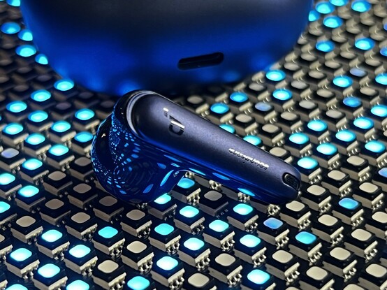 A single earbud sat atop the LEDs. It’s gloss and matte material finishes are highly contrasted. The gloss parts are reflecting the LEDs in a trippy, distorted pattern.