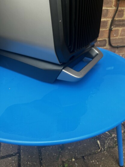 A little puddle of water spilled out onto a blue table over the batteries big chunky handle.