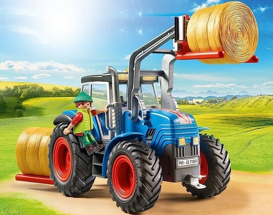 An official product photo of the old Large Tractor. It’s blue with red wheel hubs and is depicted carrying two hay bales. Large exhaust pipes are clearly visible.