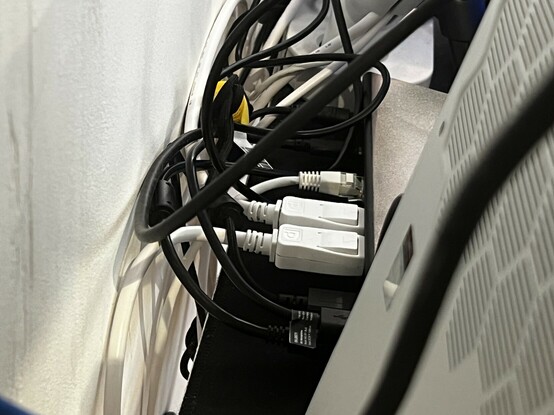 The tangle of wires behind the dock. Large, white DisplayPort connectors are plugged in with their little push button releases visible. There’s Ethernet too, and a smattering of USB cables. They all sweep behind the dock into an indecipherable tangle.