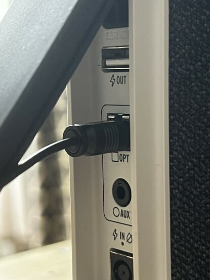 A close up of the HYPERBOOM’s inputs and outputs showing an optical cable plugged in. There’s also a bunged up service port, a USB a charging port, 3.5mm aux and a barrel jack for power.