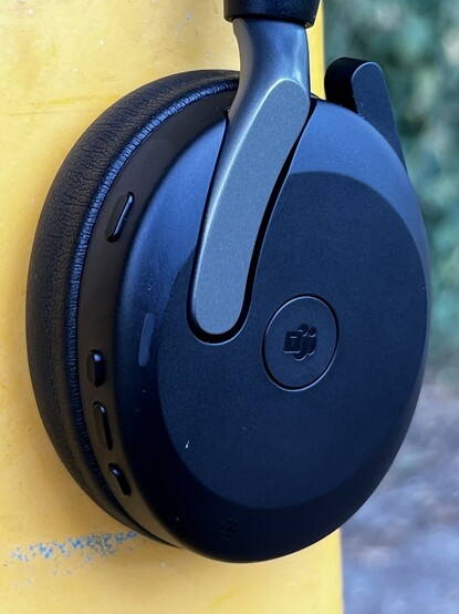The right cup of the Jabra Evolve2 65. Along the back edge are four buttons and there’s a fifth button on the side. It’s quite button heavy. The dark grey headphone is juxtaposed against a yellow post.