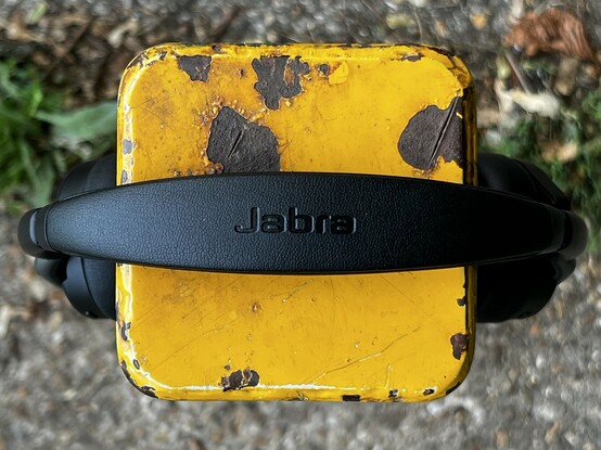 Jabra. Or at least the top of the Evolve2 65 Flex headband showing the Jabra branding. They’re hooked over a metal posted that’s painted yellow. The paint is flaking and worn.
