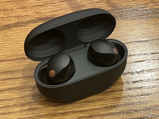 The WF-1000XM5 case with the top open revealing the two earbuds. They are a mix of matte and gloss finishes with little gold (or is it copper?) grilles presumably for the microphones. The case is matte inside and light on deals or visual clutter.
