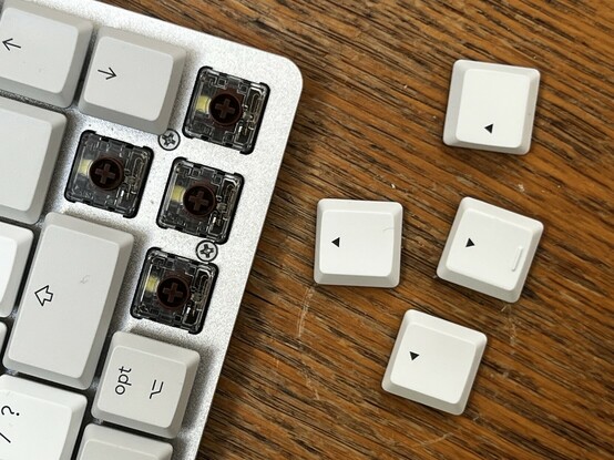 The arrow keys removed from the MX Mechanical, revealing the four brown switches underneath. A yellow LED peeks through the transparent plastic of each switch.
