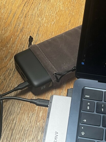 UGREEN’s 145W / 25000mAh battery in its brown sleeve connected via a short USB type C cable to a MacBook Air. A little LCD on the side shows the charge status. 99% capacity left.