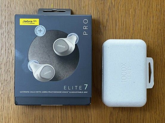 On the left is a large grey lavish cardboard box with a photo of the Elite 7 earbuds- beige and solve- and shiny lettering. It’s adorned with a sticker advertising a function added by a firmware update. On the right a much smaller recycled cardboard box for the XM5s. The external sleeve has been taken off so it’s very understated. It’s about half the total volume of the Elite 7 box.