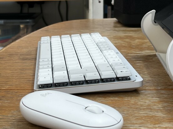 A side view of the Logitech MX Mechanical keyboard. It’s a slimline mech keyboard with white and grey low profile key caps. It’s white with a brushed metal aluminium plate underneath the keys. Very stylish.