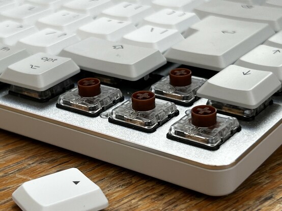 The corner of a keyboard with the three arrow keys removed revealing a T shape group of mechanical key switches. They are transparent with brown tops. They have cross-shaped - like a LEGO Technic axle - posts where the key caps connect.