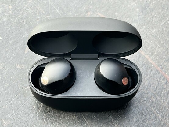 A poorly lit photo of the XM5s in their case with the lid open. The case is black and has no internal details save for recesses for the earbuds.