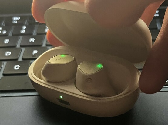 A grainy, low light and slightly motion blurred photo of me opening the Jabra Elite 7 Pro case, capturing the little LEDs - illuminated green on each - that are normally off and concealed beneath the buttons.