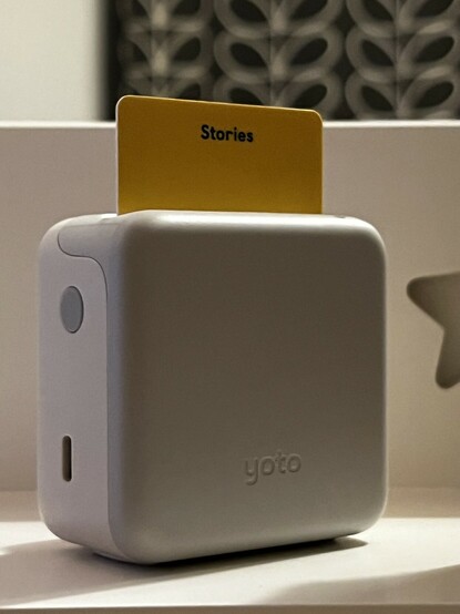 The back of the audio player, showing that the reverse of the inserted card is yellow and has “Stories” written across the top. There’s a small push button power switch on the side and a USB Type-C port below it. The back is grey plastic and has “yoto” embossed into it.