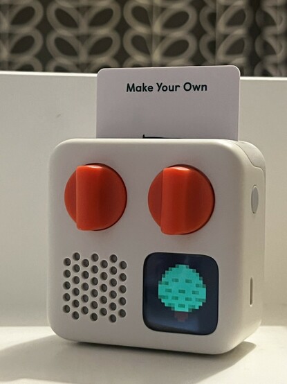 A photo of the tiny white and orange audio player with a “Make Your Own” card inserted. A pixel art tree- or maybe a small, manicured, potted shrub, but who’s counting - is shown on its screen.