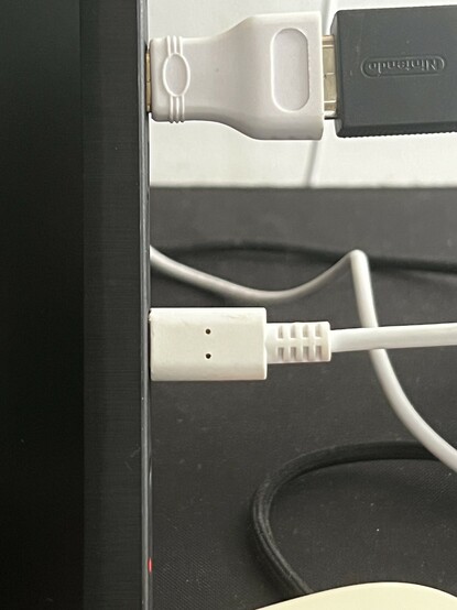 A photo of the very edge of a portable HDMI display showing two connectors plugged in- one full-sized HDMI via a small white HDMI to mini HDMI adapter and one white USB-C connector.