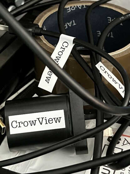 A tangled web of black cables tossed haphazardly on a desk over a roll of parcel tape. Each cable has a white label applied with “CrowView” written on it.