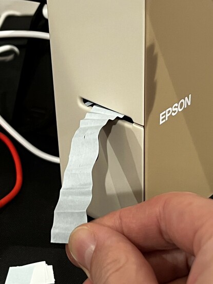 A photo of the slot on the front of the Epson LW-C610 label printer with a mangled, creased label sticking out. It’s face down so it’s not evident what the label is for.