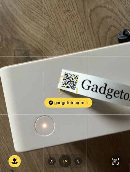A screenshot of my camera app looking at a black on white label printed with a tiny ~1cm square QR code encoding “Gadgetoid.com” my phone has detected the code and shows a little yellow bubble with the recognised domain.