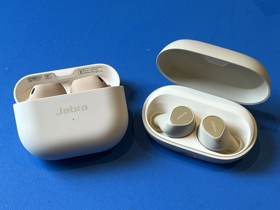 The Jabra Elite 10 next to the Elite 7 Pro. The Elite 10 case is tall and narrow, and is propped up by its flip top. The Elite 7 Pro is a squat oval, with a large lid revealing the earbuds inside a generous inner cavity.