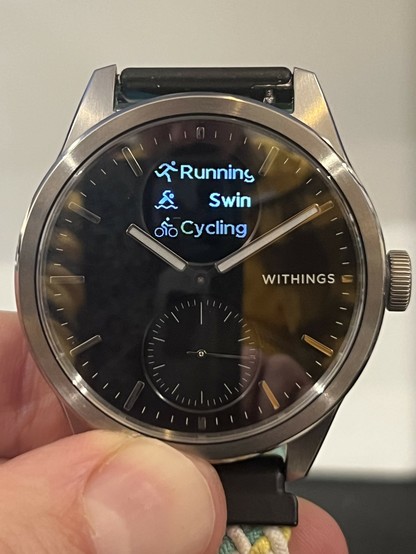 The ScanWatch 2 showing a list of exercise options. There show up on the OLED screen in a list, next to their respective icons. It’s not duper clear from the image, but the unselected items are a darker shade of grey. The selected item is “Swimming” and it’s caught mid way through scrolling the longer text across the display.
