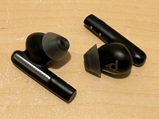 Two, black and silver earphones with oval-shaped silicon tips. They are placed next to each other, with one rotated 180 degrees in relation to the other. The in-ear portion of each is quite small, but is joined by a large stem which sticks out - like AirPods - and houses the microphones.