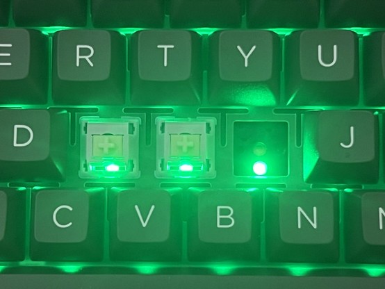 A closeup of a keyboard lit up in green showing the RTYU, DFGHJ, CVBN keys. The F and G key caps have been removed and the H cap and switch has been removed. Green LEDs shine uninterrupted - without any diffuser - through the switches and between the keys.