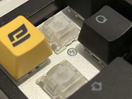 A closeup of a screw nestled at the top left of the Q key and just below 1.