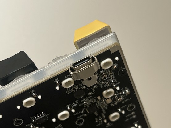 A photo of the back left corner of the KB65HEs PCB showing a USB type C connector covered with a chunky metal reinforcing plate.