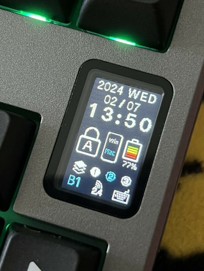 A closeup screenshot of a tiny 1” portrait OLED. At the top is the date and time, and below are a hodge podge assortment of icons indicating battery level, OS, active macro layer, connection and cap lock status.