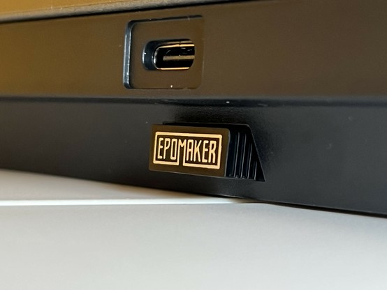 A photo of the back of the Epomaker Shadow X keyboard showing the USB Type-C port. Below is a small USB dongle protruding from a little storage nook. It has the “Epomaker” text logo on it.