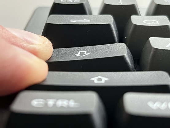 A low angle shot across the Ctrl, Shift, Capslock and tab keys of a keyboard. Shift and Caplock are being held down by their left edge. Shift is level, caps lock tilts quite a bit to the left.