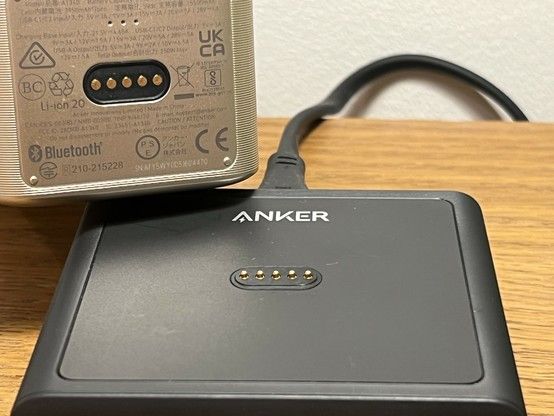 A close-up of an Anker charging base with a metallic device above it showing a set of charging connectors and various certification logos.