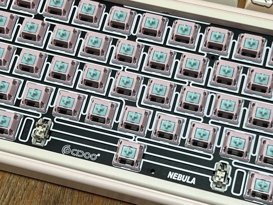 A close-up of a mechanical keyboard without keycaps, showing the pink and teal switches and the branded circuit board marked with “CIDOO” 