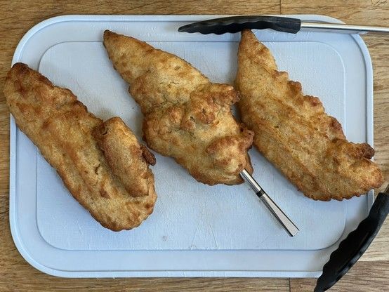 Three pieces of battered chicken on a small light blue chopping board. A silver wireless meat thermometer skewers the middle one.