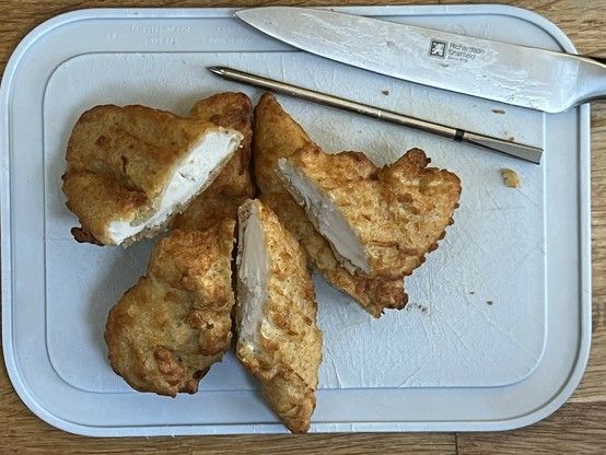 Fried chicken fillets on a small cutting board with a knife and a metal skewer-like meater thermometer sat next to them.