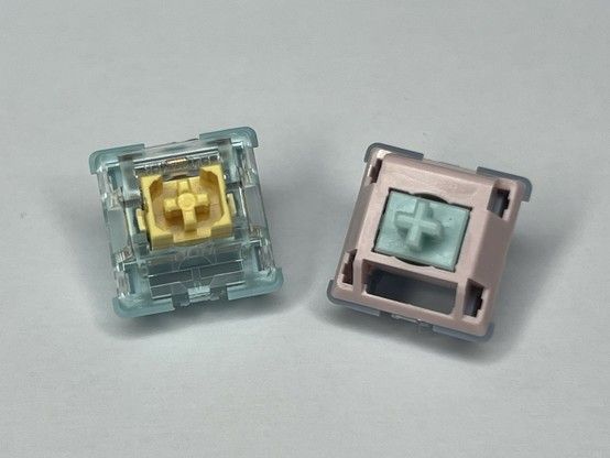Two mechanical keyboard switches on a white surface. On the left is a transparent blue and yellow “Sea Salt” switch, and on the right a pink and teal “Carda” switch. It’s quite evident that the “Sea Salt” switch is much, much better structurally while the “Carda” looks cheap.