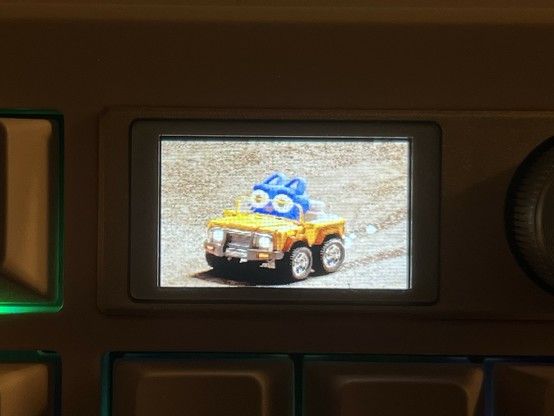A closeup of the Epomaker Shadow S LCD showing an animated gif of some kind of cartoon blue cat driving off-road in a yellow Jeep.