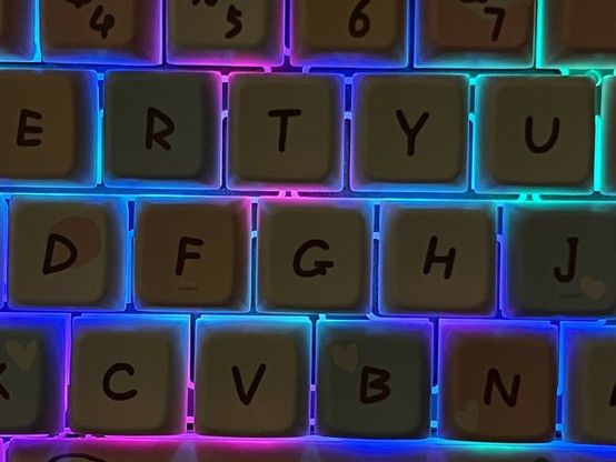 Close-up of a backlit mechanical keyboard with RGB lighting set just slightly pastel to give lovely teal pink and blue hues bleeding out between the keycaps.