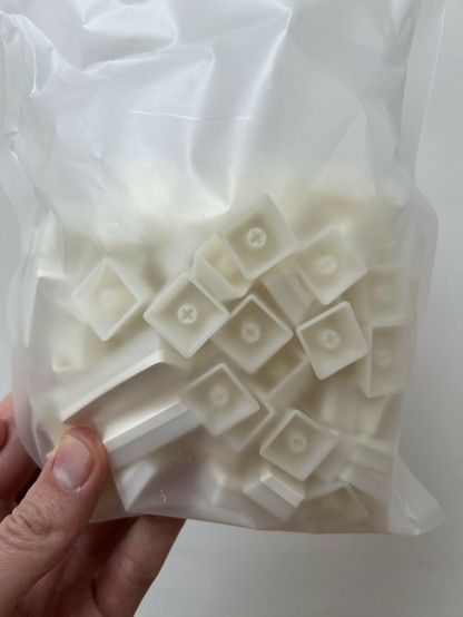 A hand holding a translucent plastic bag containing milky white keyboard keycaps.