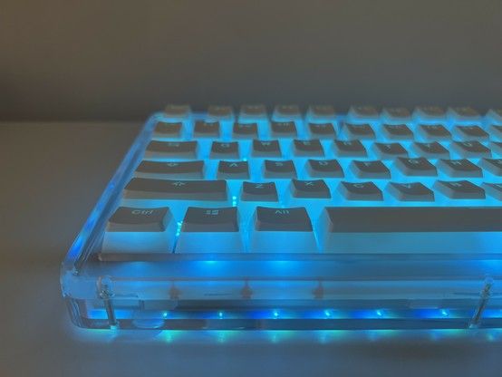 Backlit mechanical keyboard with transparent edges emitting blue light. The keys are translucent frosty white with a white cap on top- resembling Japanese “Purin” custard pudding. The sides of the keys have a pleasing diffuse glow and the legends are also clearly lit up.