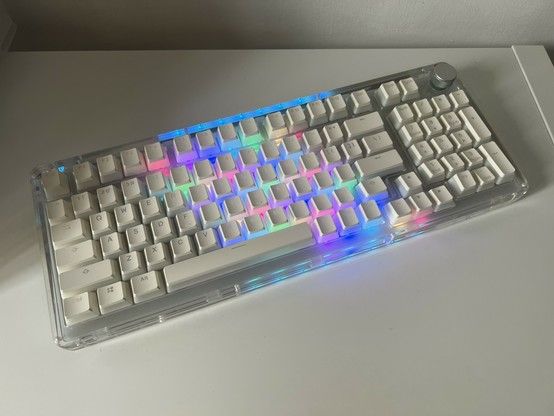 A mechanical keyboard with RGB backlighting on an Ikea Kallax shelf. The backlight is visible as a stripe across the middle of the keyboard- a matrix scan rolling shutter effect- and the frosted white keycaps are making it a pleasing diffuse pastel. It very much resembles an old Apple keyboard.